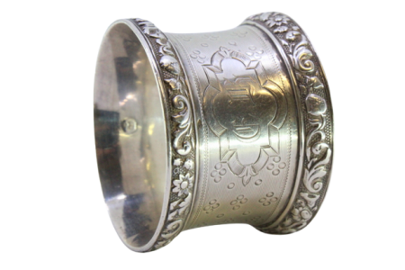 Argola de guardanapo em prata com motivos florais relevados nos frisos e guilhochada com aplicações envolvendo cartela para monograma.